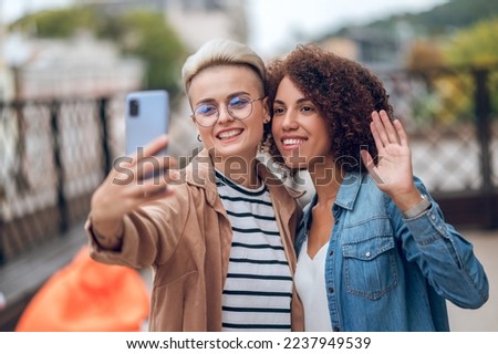 Two attractive joyous ladies taking a selfie on the veranda