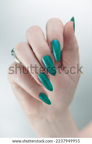 Female hands with long nails and bright green manicure with bottles of nail polish