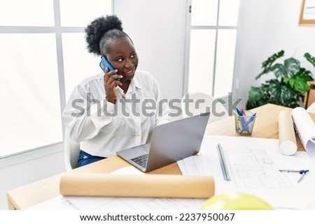Young african american woman architect using laptop and talking on the smartphone at architecture studio