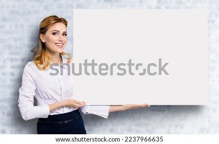 Happy excited smiling business woman in white confident clothing showing blank banner signboard. Success and advertising concept. Copy space empty place for some text. White bricks wall.