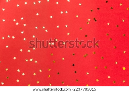 Gold sparkle confetti stars on a red background. Glitter, shine, bright. Christmas festive flat lay, winter holiday, new year, happy birthday concept. Flat lay, top view, copy space