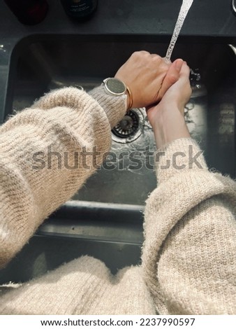 Woman washing her hands in kitchen sink. She is wearing a woolen sweater and a sport watch.