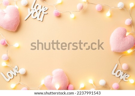 Valentine's Day concept. Top view photo of fluffy heart shaped toys inscriptions love you light bulb garland and soft pompons on isolated pastel beige background with blank space in the middle