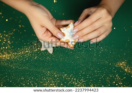 Women's hands hold a handmade gingerbread on a green background. Festive manicure.
