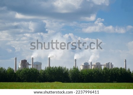 Tall chimneys of a factory with smoke rising up, polluting the atmosphere. Concept of air pollution, ecological environment.  Royalty-Free Stock Photo #2237996411