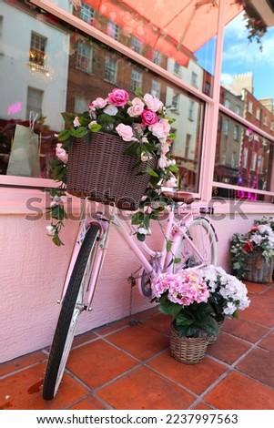 A flower filled basket in a pink bike in front of a pink café