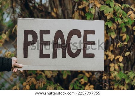 Protest against war with banner placard  with inscription message text PEACE, autumn tree  background. Crisis, peace, aggression invasion concept. anti-war demonstration.