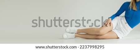 cropped view of woman with slender legs posing in white shorts and sneakers on grey background, banner