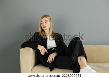 Pretty woman in jacket looking away while sitting on couch at home