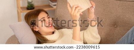 Young asian woman wearing sweater and reading a book while lying to relaxation in holiday on sofa in cozy living room of christmas decoration at home.