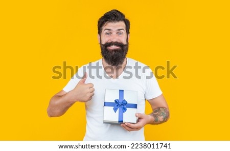 birthday man holding present box. thumb up. bearded man with present box in studio.