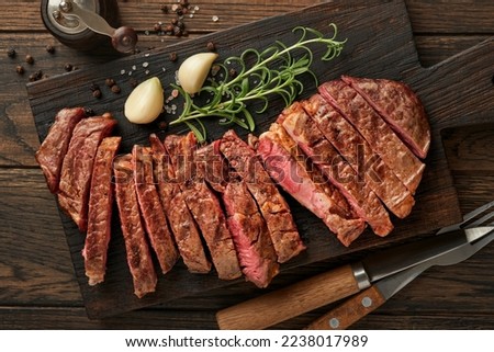 Steaks. Sliced grilled meat steak New York or Ribeye with spices rosemary and pepper on black marble board on old wooden background. Top view. Mock up. Royalty-Free Stock Photo #2238017989
