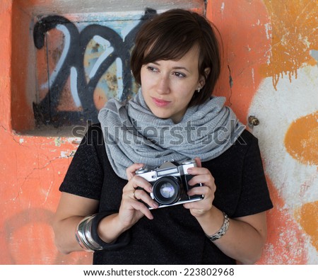 A beautiful girl with a retro single-lens reflex mirror camera near the graffiti wall
