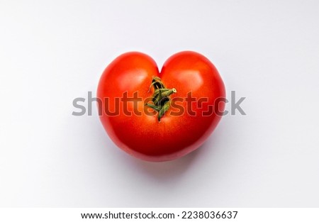 Wonky shaped red tomato in the shape of a heart shot from above on a white surface. Royalty-Free Stock Photo #2238036637
