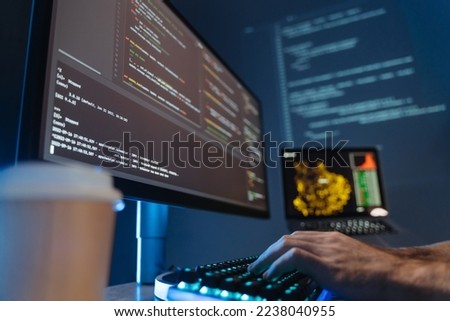 No face picture of male hands of software engineer sitting at table in front of big pc screen, typing and composing app script, working in data science company. Selective focus