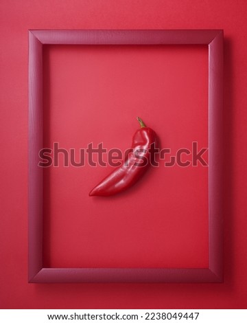 Whole red pepper in wooden picture frame on red background