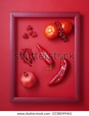 Pomegranate, pepper, raspberry, currant and tomato in wooden picture frame on red background