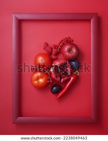 Pomegranate, pepper, raspberry, currant, apple, plum and tomato in wooden picture frame on red background