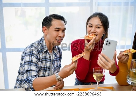Happy and joyful Asian female taking selfie with her phone while enjoy eating pizza in the party with her friends. New year party, corporate party, pizza party at home.