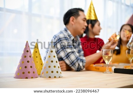 Colorful party hats on the table over blurred background of a group of friends talking and having fun in the party.