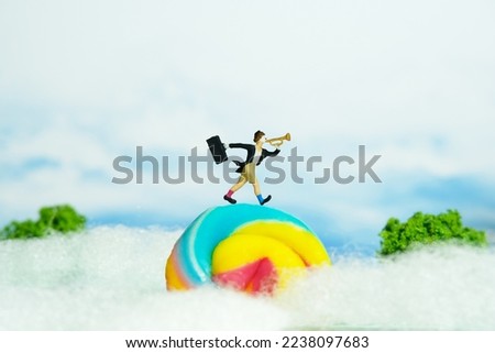 Miniature people toy figure photography. Playground island above clouds. A clown wearing black suit and hat blow the trumpet walking above rainbow candy. Image photo