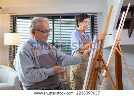 Couple Senior drawing at art. Side view portrait of white haired senior woman holding palette painting pictures at easel in art studio.