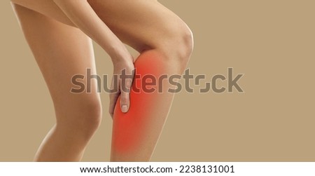 Sick or injured woman experiencing calf muscle pain standing isolated on beige background. Close up of woman's leg with injury caused by sports accident or arthritis, sore spot is marked in red Royalty-Free Stock Photo #2238131001