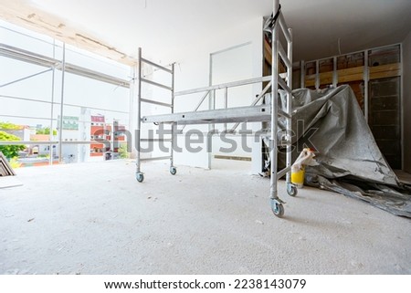 Mobile metal scaffolding with small wheels and protective helmet on it placed in the building under construction. Work is in progress.   Royalty-Free Stock Photo #2238143079