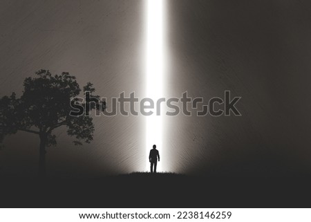 A silhouette of a man in nature next to a tree, walking towards a bright light in the opened huge wall. A light in the end of a tunnel. The concept of success, freedom, choice, open mind, meditation. Royalty-Free Stock Photo #2238146259