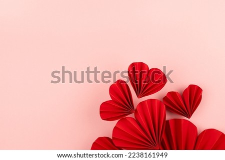 Red paper ribbed hearts fly as flow on soft light pink background as festive Valentine day background, top view, copy space.