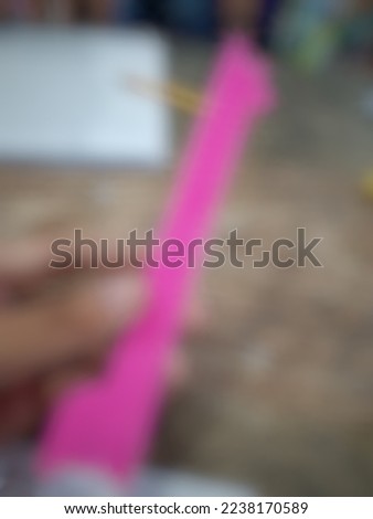 Defocused or blurred abstract background of a pink plastic ruler owned by most students and it is hold by a left hand