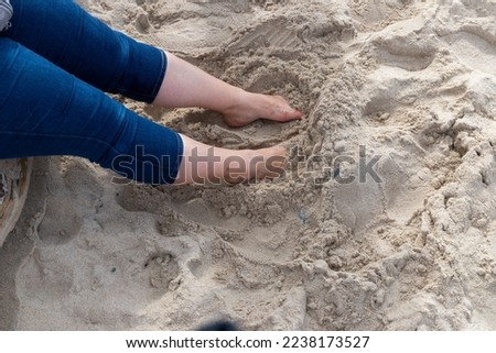 Women's foot with jeans and red nail polish in the sand. High quality photo