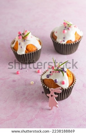Easter cupcakes with white icing, pink and purple sprinkles and green decor on a pink concrete background. Easter concept. Holidays, parties