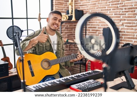 Young hispanic man doing online guitar tutorial smiling happy and positive, thumb up doing excellent and approval sign 