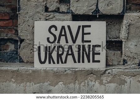 Ukrainian protest against war with banner placard  with inscription message text Save Ukraine, ruined city background. Crisis, peace, Russian aggression invasion concept. anti-war demonstration.