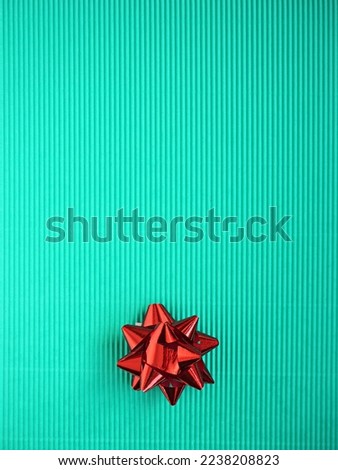 Realistic blue, green, turquoise cardboard background texture. Christmas greeting card craft paper with red shiny bow. Top view, flat lay, copy space for New Year poster, banner.