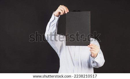 Empty black board A4 paper in man hand covered face and wear blue shirt on black background.