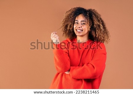 Happy young black woman playing with her curly hair and looking at camera in studio shot against brown background. Royalty-Free Stock Photo #2238211465