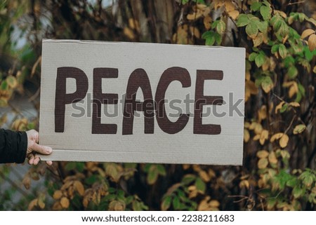 Protest against war with banner placard  with inscription message text PEACE, autumn tree 
 background. Crisis, peace, aggression invasion concept. anti-war demonstration.