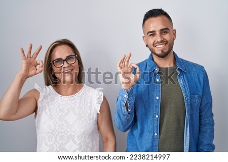 Hispanic mother and son standing together smiling positive doing ok sign with hand and fingers. successful expression. 