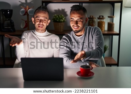 Homosexual couple using computer laptop smiling cheerful offering palm hand giving assistance and acceptance. 