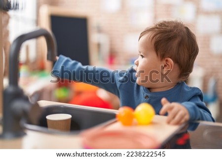 Adorable caucasian baby playing with play kitchen standing at kindergarten