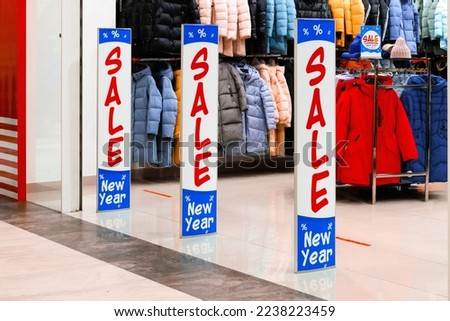 A red, white, and blue banner on an anti-theft gate sensor at the entrance to a retail mall. Sale in a winter clothing store. Warm down jackets in different colors.