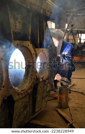 A worker welding metal parts on a construction site. A welder welds parts of a large machine in a metallurgical workshop.. An interesting example of manual work.