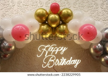Happy Birthday decoration at the venue. White, pink, silver and gold colored baloons, lit Happy birthday signage on the designer wall.
