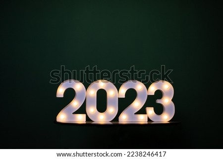 New Year's background, 2023 numbers, lights glowing on a dark monochromatic green background, holidays, minimalism card, screensaver. happy new year and christmas concept