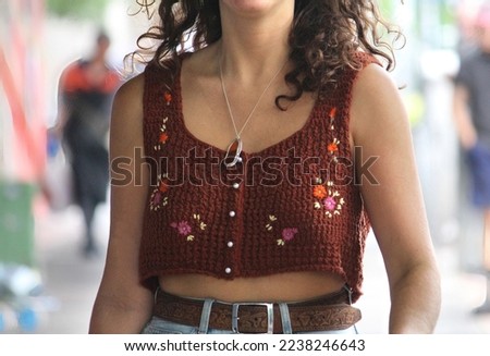 Young woman wearing a brown crochet crop top with flowers on it walking down the street