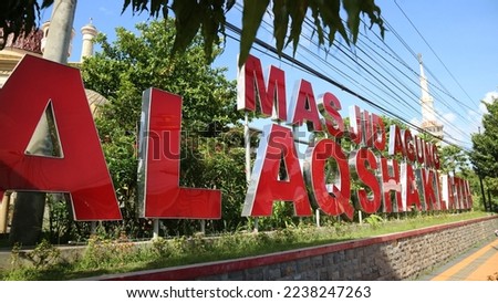 Sign board Name of Masjid Agung Al-Aqsha Klaten on the blue sky background on the side of the street. Red Color.