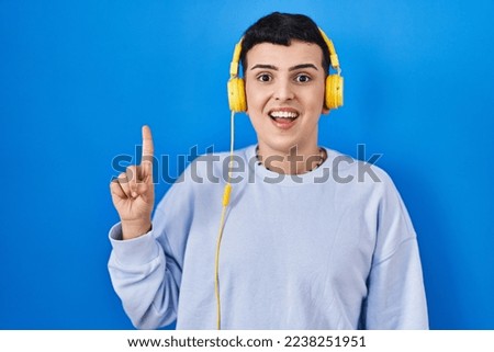Non binary person listening to music using headphones pointing finger up with successful idea. exited and happy. number one. 