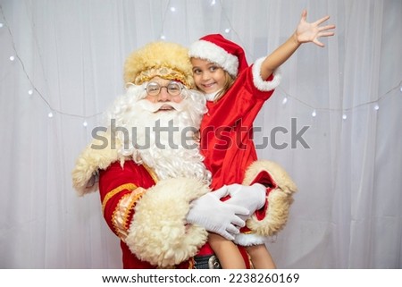 Beautiful happy child on Santa's lap. Photo of a bearded santa claus holding a small little girl on his lap